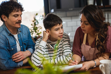 Latino boy doing his homework with the help of computer and his parents.