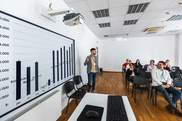 Male CEO standing in front of a multiracial group of colleagues. Multimedia classroom with smart...