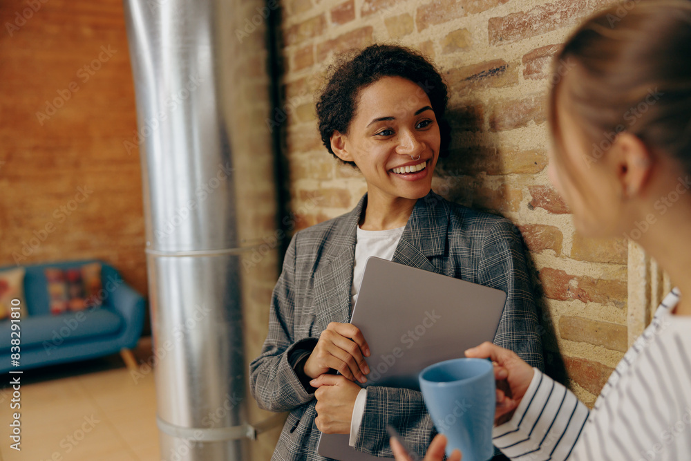 Wall mural Young diverse female employees is talking and drink coffee during break time in stylish office