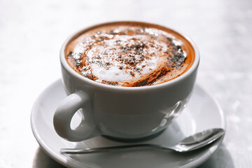 A cup of coffee with a spoon on a saucer, ready to be enjoyed and savored. Morning hot drink