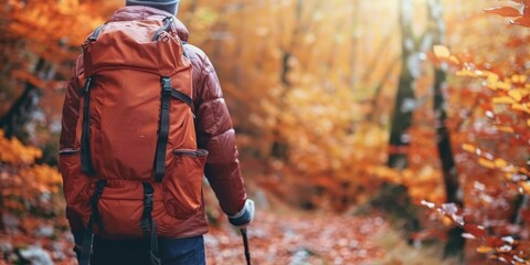 The photo shows a person hiking in the woods during the fall season. The person is wearing a backpack and there are trees with orange and yellow leaves all around.