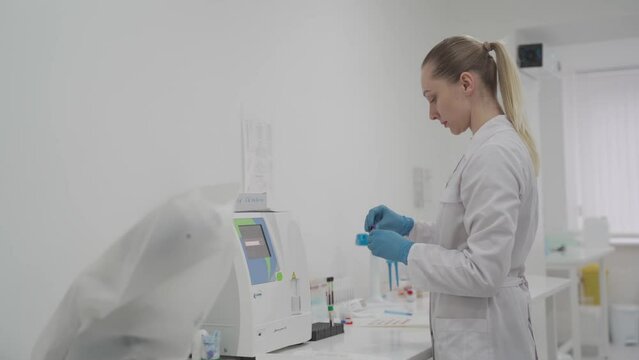 Female laboratory technician using hematology blood analyzer. Medical equipment in lab. Biochemical and hematological analysis of blood. Automatic blood test analyzer in medical laboratory
