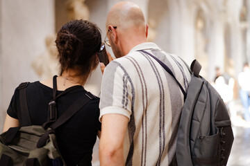 Rear view of father and daughter with backpacks sharing the audio guide in a museum.