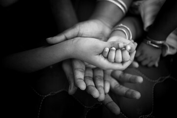 hands of family members holding hands of just born baby shot in black and white- monochrome picture