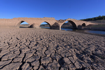 Medieval bridge under a blue sky in the Aguilar de Campoo reservoir that is only seen in times of...