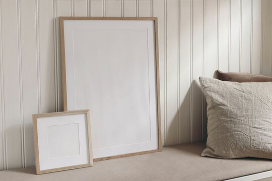 Set of blank portrait and square wooden picture frame mockups. Bench with beige linen, velvet cushions, pillows. White wooden beadboard wall panelling background. Elegant home interior decor still