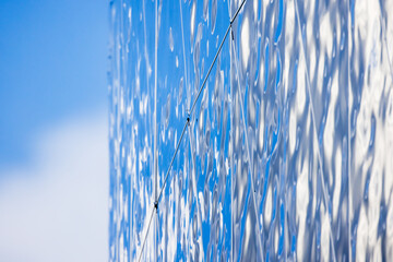Shiny blue metal wall made of rippled steel plates reflects cloudsy sky