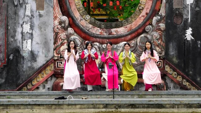 Hoi An, Da Nang - March 2, 2024: Beautiful girls in national Vietnamese dresses pose taking photos on the phone