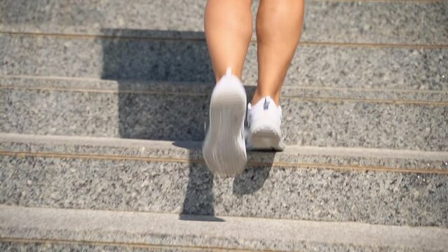 Close-up female teenager girl legs with sport shoes sneakers climd step the stairs. Rear view. Woman hurry up walking staircase sunny warm weather outdoors