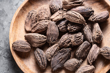 Indian spice black cardamom in wooden plate on gray background close-up