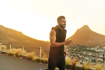 Sunset, man and running with smile in countryside for fitness and exercise in summer. Mountain, athlete and training for marathon in nature for wellness and workout with happiness or pride in France