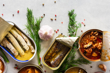 Different open tin cans with canned fish among spices and herbs, canned salmon and mackerel, sprat...