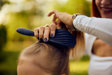 Close-up photo of a mothers hands making a hairstyle to her daughter, using a comb, at the park.