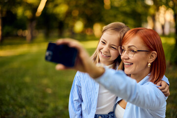 Smiling mother and daughter taking photos with a mobile phone at the park.