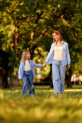 Fototapeta premium Mother and daughter with matching outfits walking through the park, holding hands, smiling.