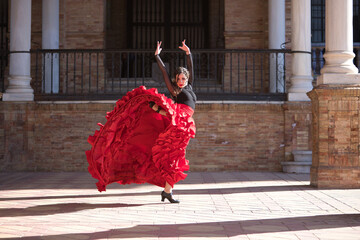 Young, beautiful, brunette woman in black shirt and red skirt, dancing flamenco between marble...
