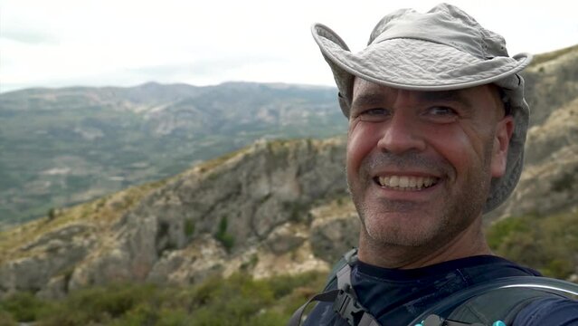Slow motion, smiling hiker takes a video selfie looking at camera, showing the landscape on background