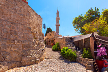 Stone pathway leading to historic minaret with surrounding stone wall and greenery in Rhodes, Greece