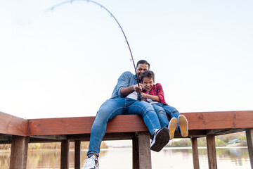 African American man and child sitting on a wooden pier holding fishing rods on the river, dad teaching his son to fish in the lake, family resting and relaxing on the weekend