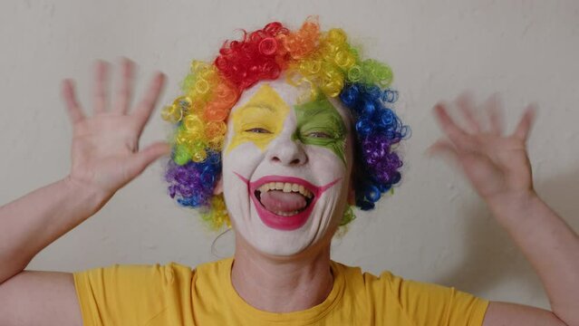 Funny clown is having fun and grimacing face while looking at camera. Cheerful harlequin makes people laugh.