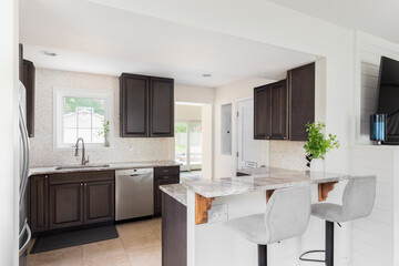 A kitchen with dark brown wood cabinets, granite countertop, chairs sitting at a bar top island, and hardwood flooring. No brands or labels.