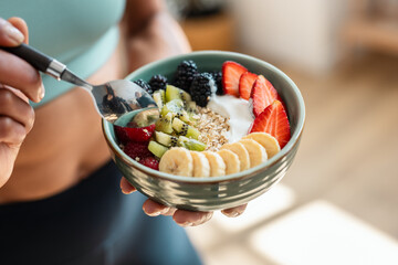 Mature athletic woman eating a healthy fruit bowl in the kitchen at home