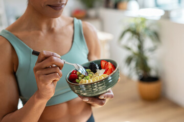 Mature athletic woman eating a healthy fruit bowl in the kitchen at home