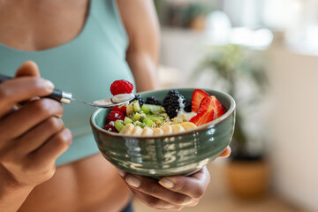 Mature athletic woman eating a healthy fruit bowl in the kitchen at home