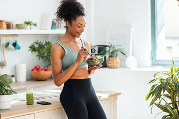 Athletic woman eating a healthy fruit bowl in the kitchen at home