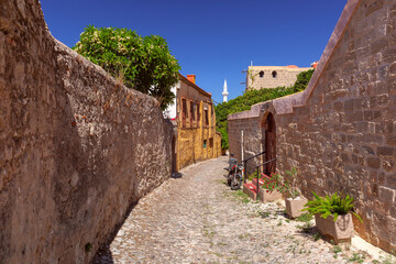 Narrow cobblestone street in Old Town of Rhodes Greece with stone walls and minaret in background
