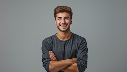 A handsome young man smiling with his arms crossed against a grey background, wearing casual with a confident and happy expression in a studio portrait. - Powered by Adobe