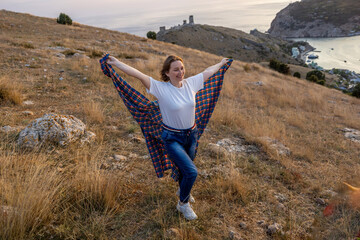 A woman is standing in a field with a blanket draped over her shoulders. She is smiling and she is...