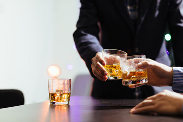 A group of businessmen held brandy glasses together to cheers glasses of brandy after concluding negotiations on business ventures and reaching a satisfactory agreement for joint business profits.