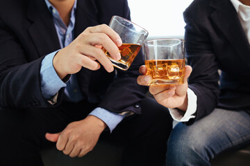 A group of businessmen held brandy glasses together to cheers glasses of brandy after concluding negotiations on business ventures and reaching a satisfactory agreement for joint business profits.