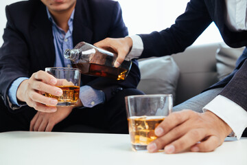 Businessmen and investors drink alcohol together in office after discussing their joint venture...