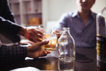 A group of businessmen held brandy glasses together to cheers glasses of brandy after concluding negotiations on business ventures and reaching a satisfactory agreement for joint business profits.