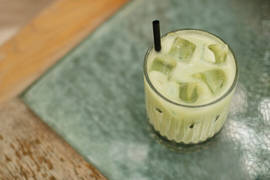A matcha latte with ice served in a beautiful glass on a terrace table in a city cafe. Summer refreshing drink.