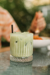 A matcha latte with ice served in a beautiful glass on a terrace table in a city cafe. Summer refreshing drink.