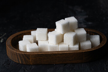Sugar cubes in wooden tray on dark background, showcasing their purity and neat arrangement in center attention.