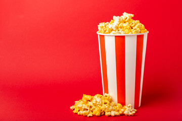 Popcorn box. Red and white striped buckets of popcorn on a red background. Cinema and entertainment concept. Movie night with popcorn. Cheesy popcorn. Delicious appetizer, snack. Place for text.
