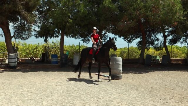 close-up of jockey sitting on horse. young woman riding brown horse at demonstration competition in sandy parkour arena. competitive rider gallops in an outdoor training arena. Equestria