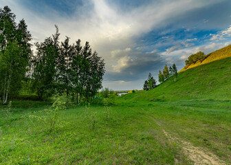 Obraz premium A picturesque path winds through a grassy meadow, leading toward a distant valley bathed in the warm glow of a spring day.