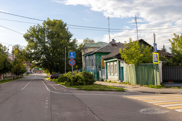 An empty street in a small Russian town with colorful houses and a pedestrian crosswalk. The sky is blue with a few clouds..