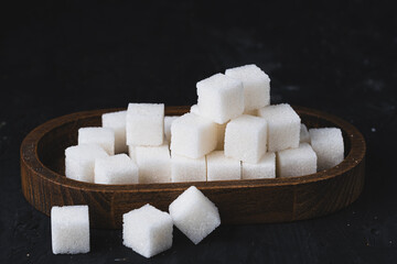 Sugar cubes in a wooden bowl on black background.