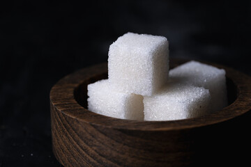 Sugar cubes in a wooden bowl on a dark background.