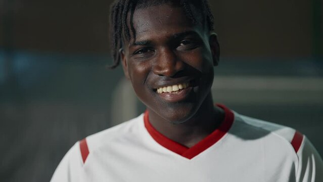 Happy young black soccer player playing with ball on indoors field, portrait. African American athletic man throwing ball, hitting by head, smiling and laughing, workout of professional football team