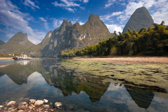 A river cruise ship sailed through the most beautiful tourist destination with bamboo trees and gentle slope mountains along the bank of Li River in Yang Shuo, Guangxi province,  Southern China.