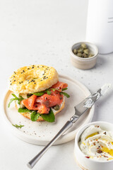 Homemade bagel sandwich with smoked salmon, cream cheese, capers and spinach for healthy breakfast on white kitchen background, text space