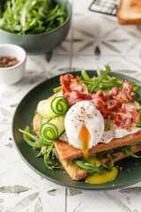 Toasts sandwich with poached egg, cucumber, arugula, bacon and cream cheese on printed tile kitchen background for healthy breakfast