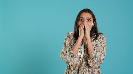 Anxious indian woman covering face with palms, worried about future, isolated over studio...